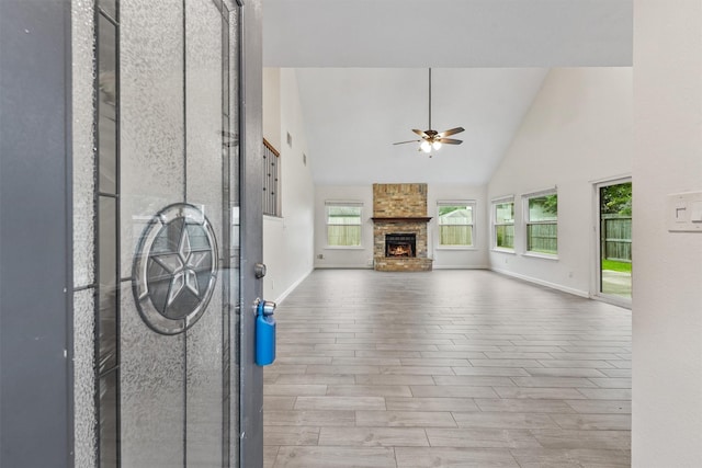 unfurnished living room with a ceiling fan, baseboards, wood finished floors, high vaulted ceiling, and a large fireplace