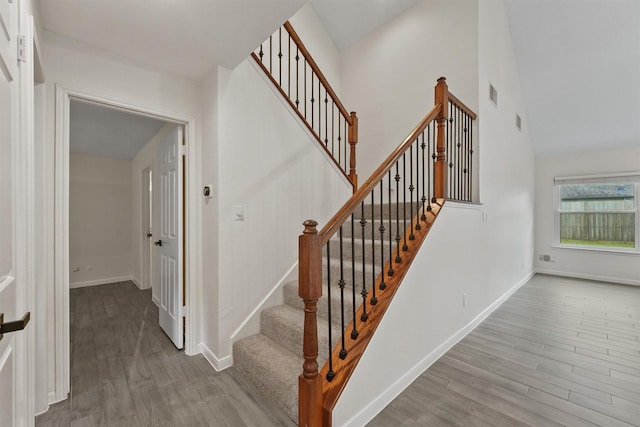 staircase with wood finished floors, baseboards, and high vaulted ceiling