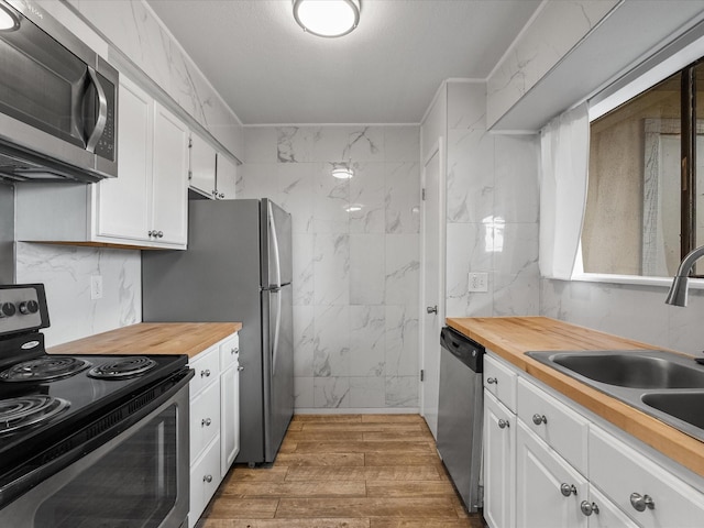 kitchen with appliances with stainless steel finishes, butcher block counters, a sink, white cabinets, and wood finished floors