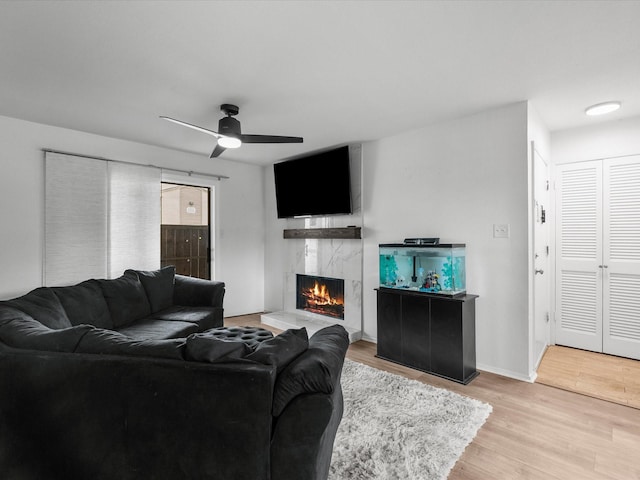 living area featuring a fireplace, ceiling fan, light wood-type flooring, and baseboards