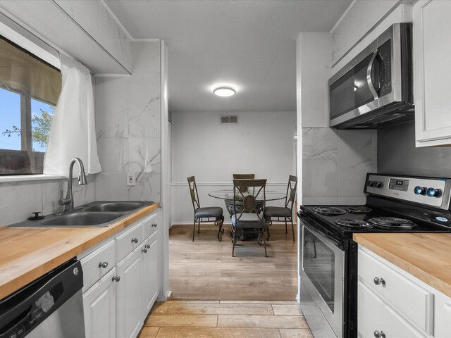 kitchen featuring appliances with stainless steel finishes, a sink, wooden counters, and light wood-type flooring