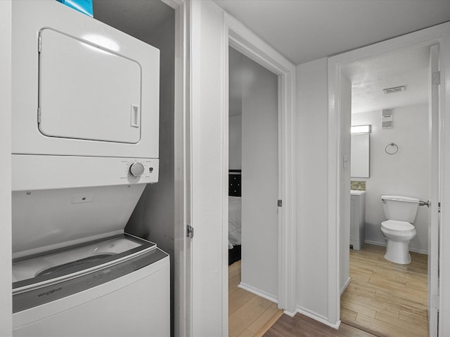 laundry room with stacked washing machine and dryer, wood finished floors, and baseboards