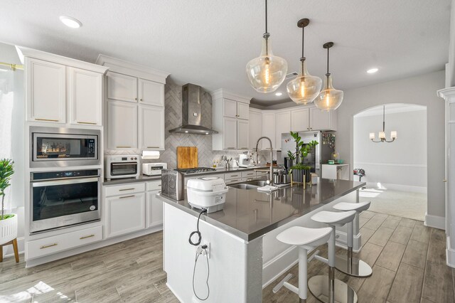 2723 Camellia Ave, Brookshire, TX 77423 - kitchen featuring stainless steel appliances, wall chimney exhaust hood, a sink, dark countertops, and arched walkways