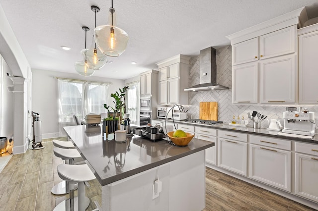 2723 Camellia Ave, Brookshire, TX 77423 - kitchen featuring wall chimney exhaust hood, appliances with stainless steel finishes, dark countertops, backsplash, and light wood finished floors