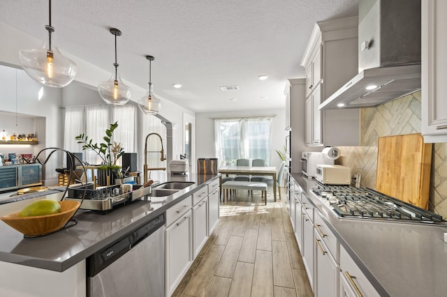 2723 Camellia Ave, Brookshire, TX 77423 - kitchen featuring stainless steel appliances, wall chimney exhaust hood, dark countertops, a sink, and a center island with sink