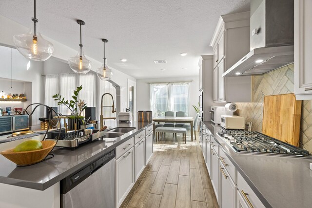 2723 Camellia Ave, Brookshire, TX 77423 - kitchen with wall chimney range hood, stainless steel appliances, dark countertops, a kitchen island with sink, and tasteful backsplash