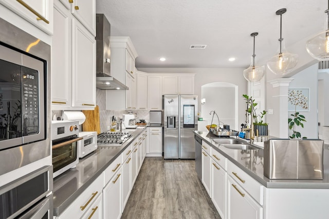 2723 Camellia Ave, Brookshire, TX 77423 - kitchen featuring appliances with stainless steel finishes, wall chimney range hood, a center island with sink, arched walkways, and white cabinets
