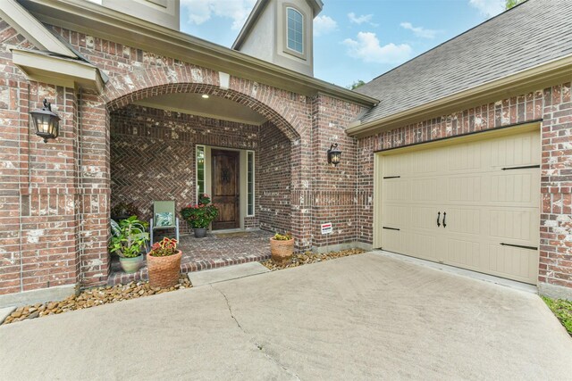 view of exterior entry with concrete driveway, brick siding, a shingled roof, and a garage