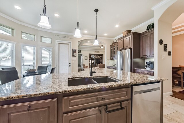kitchen with stainless steel appliances, arched walkways, a sink, a center island with sink, and ornamental molding
