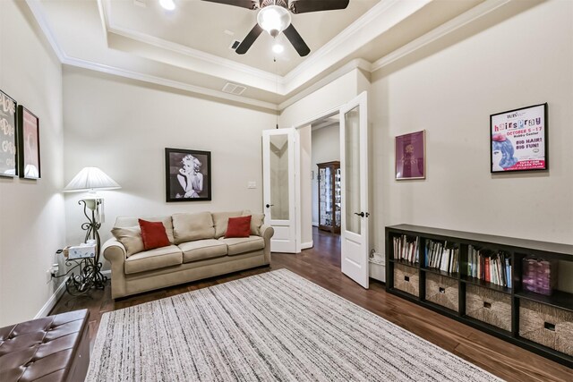 living area with crown molding, a tray ceiling, dark wood-type flooring, ceiling fan, and baseboards