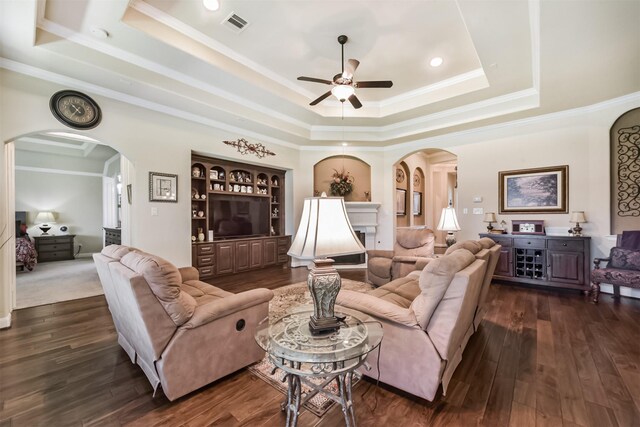 living room with arched walkways, a raised ceiling, a ceiling fan, crown molding, and dark wood-style flooring