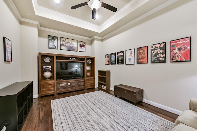 living room featuring a tray ceiling, dark wood-style flooring, crown molding, ceiling fan, and baseboards