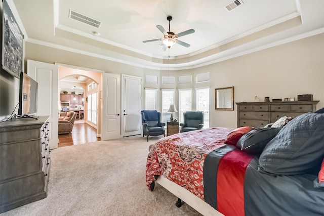 carpeted bedroom with a tray ceiling, crown molding, arched walkways, and a ceiling fan