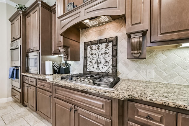 kitchen featuring appliances with stainless steel finishes, decorative backsplash, light stone counters, baseboards, and crown molding