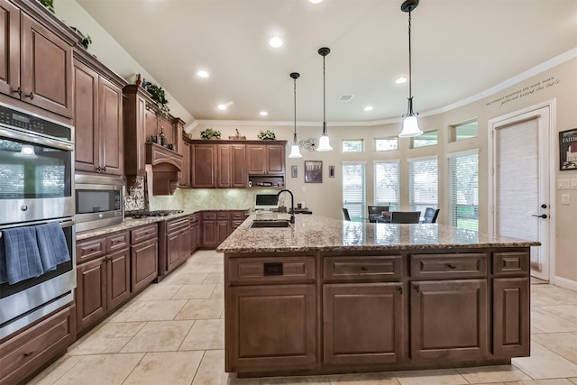 kitchen with appliances with stainless steel finishes, a kitchen island with sink, ornamental molding, tasteful backsplash, and a sink