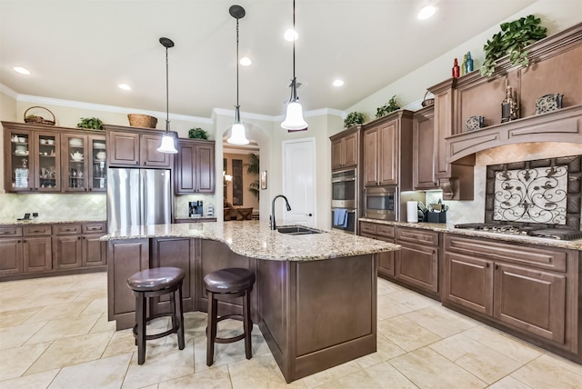 kitchen with stainless steel appliances, a sink, backsplash, crown molding, and an island with sink