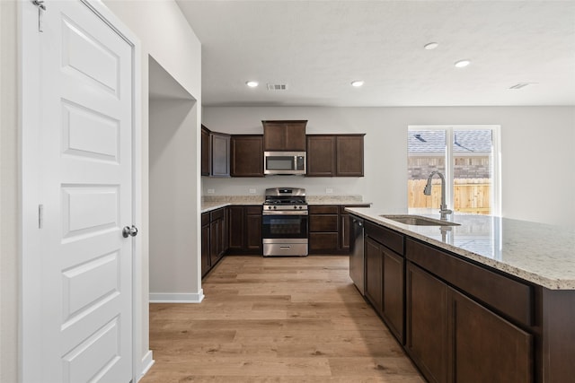 3021 Pampaneria Dr, Conroe, TX 77301 - kitchen featuring appliances with stainless steel finishes, a sink, light wood-type flooring, dark brown cabinetry, and recessed lighting