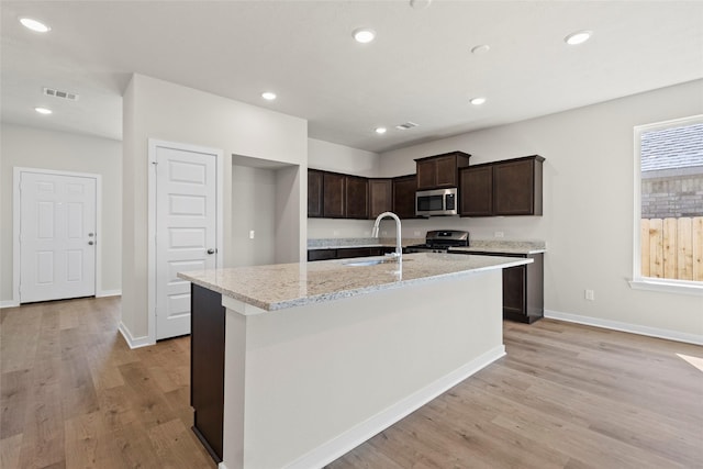 3021 Pampaneria Dr, Conroe, TX 77301 - kitchen with appliances with stainless steel finishes, a sink, dark brown cabinetry, light wood finished floors, and baseboards