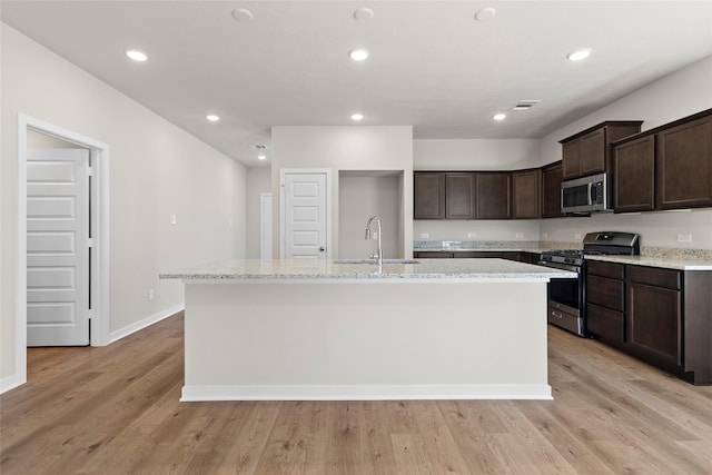 3021 Pampaneria Dr, Conroe, TX 77301 - kitchen with appliances with stainless steel finishes, a sink, an island with sink, dark brown cabinets, and light wood finished floors