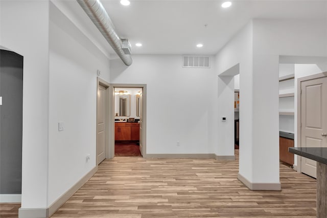 spare room featuring light wood-style floors, recessed lighting, baseboards, and arched walkways