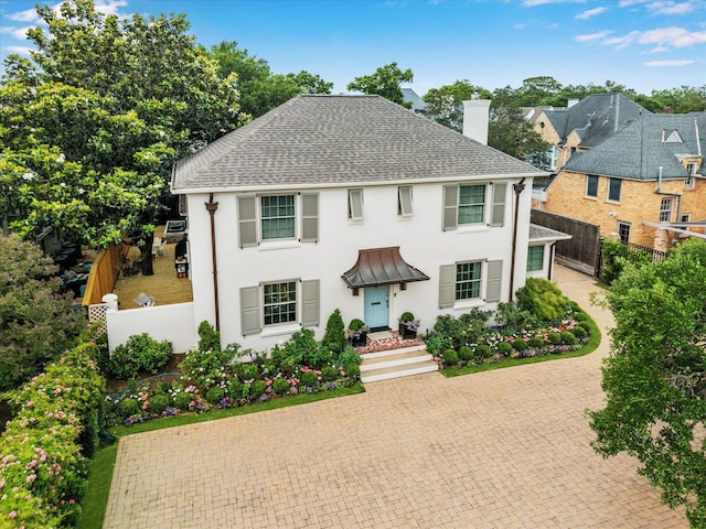 colonial home featuring a chimney, a shingled roof, fence, and decorative driveway
