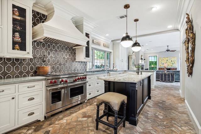 kitchen featuring range with two ovens, custom range hood, ornamental molding, brick floors, and tasteful backsplash