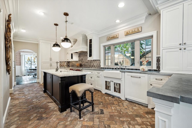 kitchen with custom range hood, brick flooring, a sink, crown molding, and decorative backsplash
