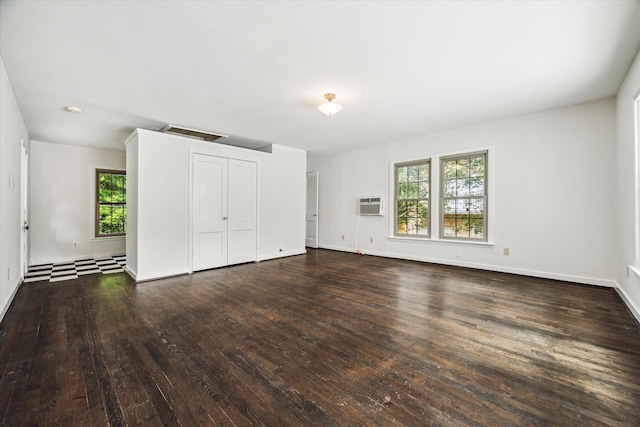 unfurnished bedroom with dark wood-type flooring, baseboards, an AC wall unit, and a closet