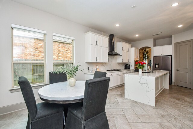 kitchen featuring wall chimney range hood, white gas cooktop, white cabinets, recessed lighting, and an island with sink