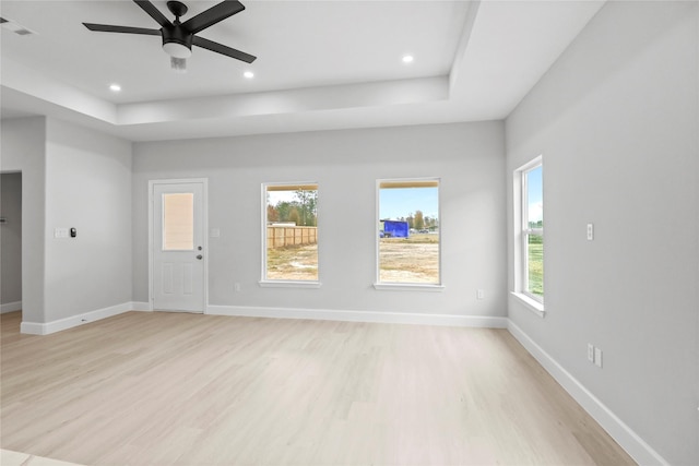 unfurnished living room featuring light wood-style floors, ceiling fan, recessed lighting, baseboards, and a tray ceiling
