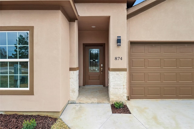 entrance to property with stucco siding, a garage, concrete driveway, and stone siding