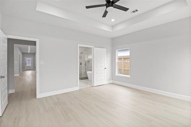 unfurnished bedroom with a raised ceiling, light wood finished floors, baseboards, recessed lighting, and ensuite bathroom