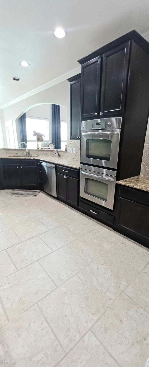 kitchen with stainless steel appliances, dark cabinetry, ornamental molding, recessed lighting, and a sink