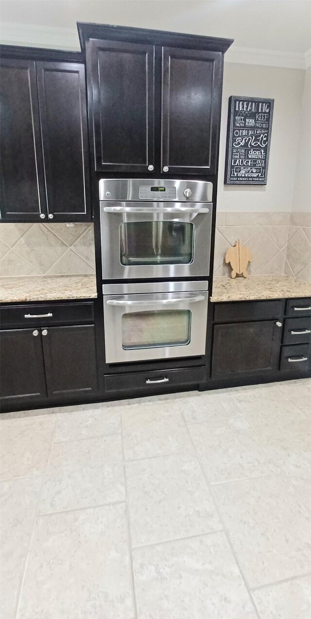 kitchen with ornamental molding, backsplash, double oven, dark cabinetry, and light tile patterned flooring