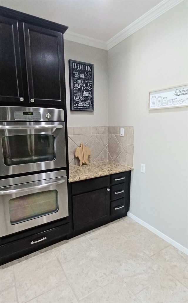 kitchen featuring dark cabinets, stainless steel double oven, crown molding, backsplash, and baseboards