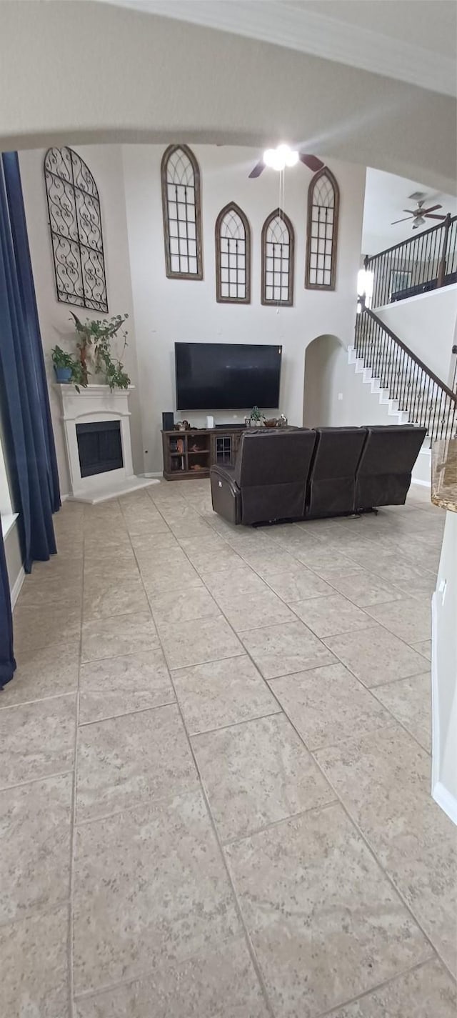 living area with a ceiling fan, a fireplace, ornamental molding, and stairs