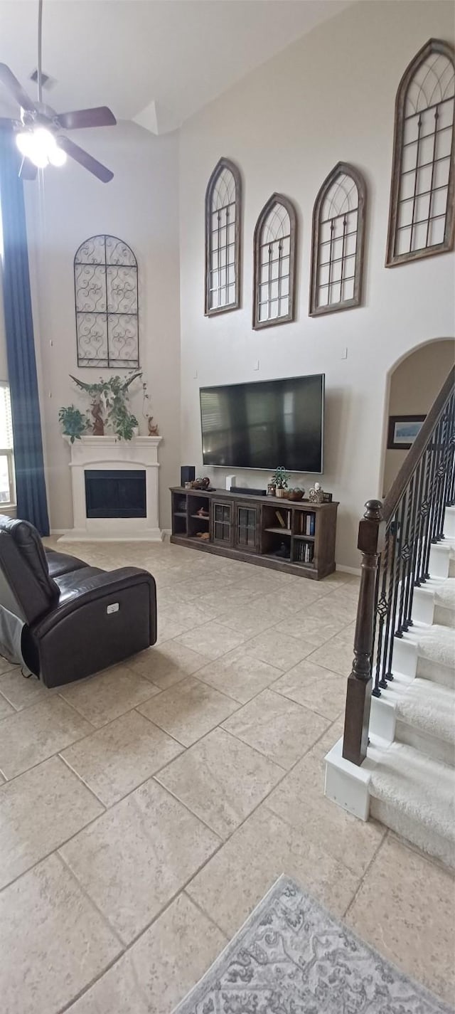 living area featuring ceiling fan, a fireplace, a towering ceiling, stairway, and baseboards