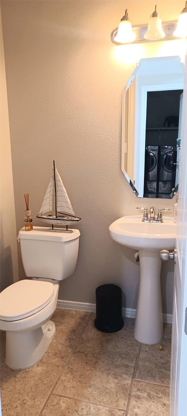 bathroom featuring washer and dryer, toilet, and baseboards