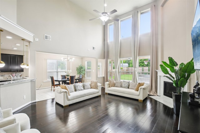 living area with a towering ceiling, a premium fireplace, ceiling fan, dark wood-type flooring, and a chandelier