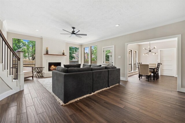 living area featuring ornamental molding, a fireplace, stairs, dark wood finished floors, and a chandelier