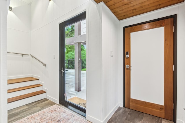 entryway with baseboards, wood finished floors, wooden ceiling, stairs, and crown molding