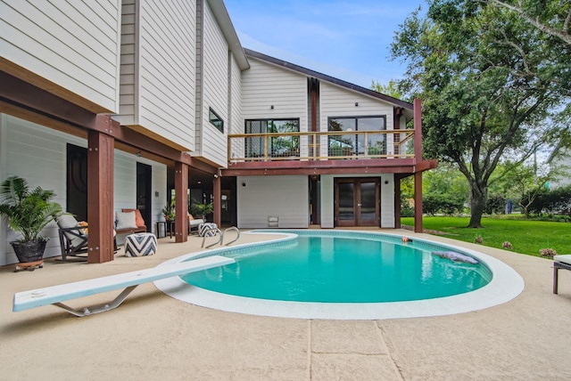 swimming pool featuring french doors, a diving board, a patio area, and a lawn