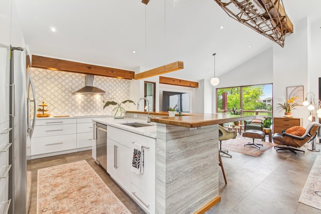 kitchen featuring wall chimney range hood, decorative backsplash, modern cabinets, a sink, and white cabinets