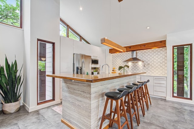 kitchen featuring stainless steel appliances, wall chimney range hood, modern cabinets, backsplash, and light countertops