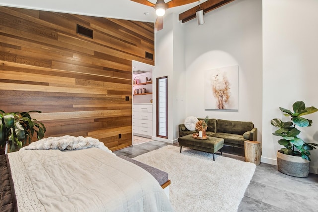 bedroom with wooden walls, a towering ceiling, beamed ceiling, an accent wall, and baseboards