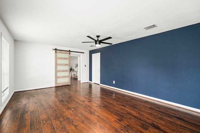 empty room featuring a barn door, ceiling fan, wood finished floors, and baseboards