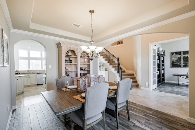 dining room featuring a raised ceiling, arched walkways, stairway, a chandelier, and ornamental molding