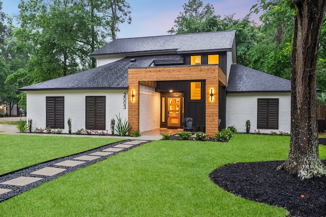 contemporary house with a shingled roof, brick siding, and a yard