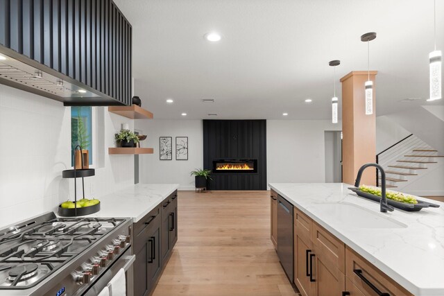 kitchen featuring stainless steel appliances, a sink, open shelves, wall chimney exhaust hood, and light wood-style flooring
