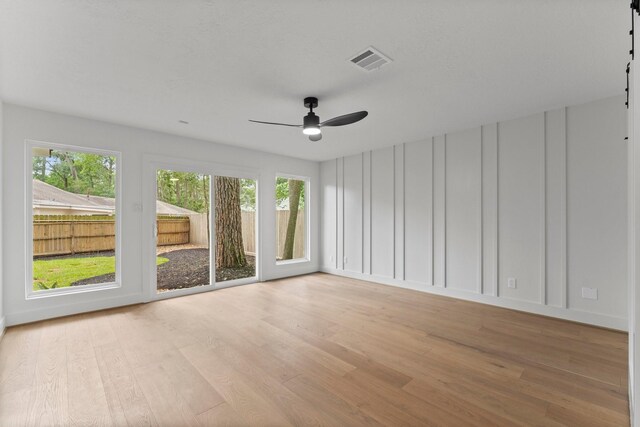 empty room with light wood-type flooring, plenty of natural light, a ceiling fan, and a decorative wall